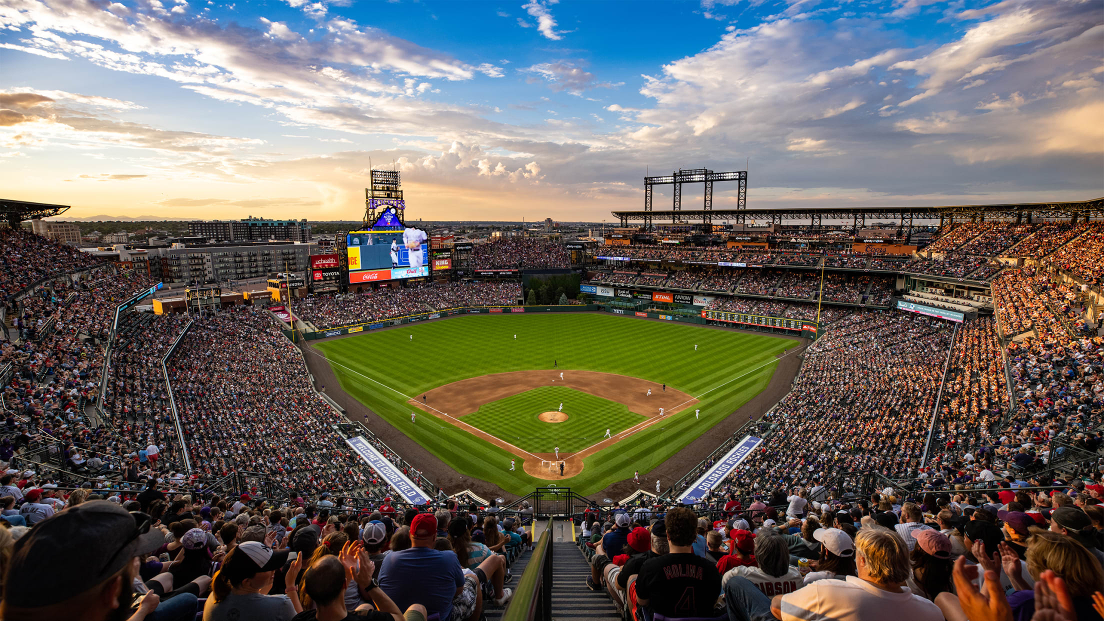 View of home plate from the 3rd level on a summer night with the sunset and full ballpark watching the Colorado Rockies