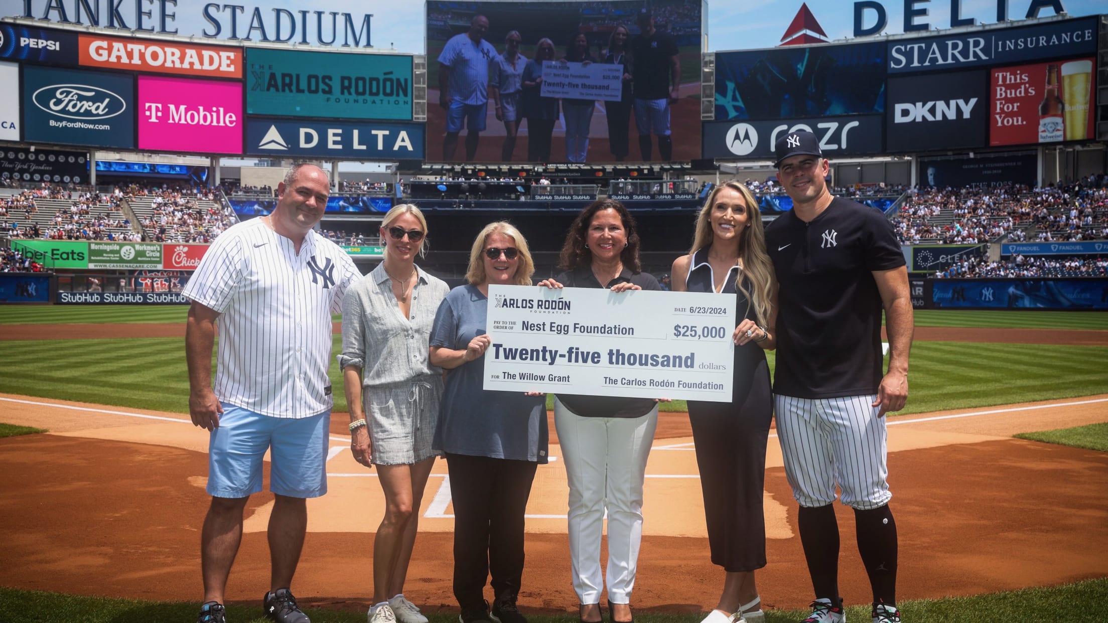 Carlos Rodón and others pose behind home plate at Yankee Stadium with a giant check for $25,000 to the Nest Egg Foundation.