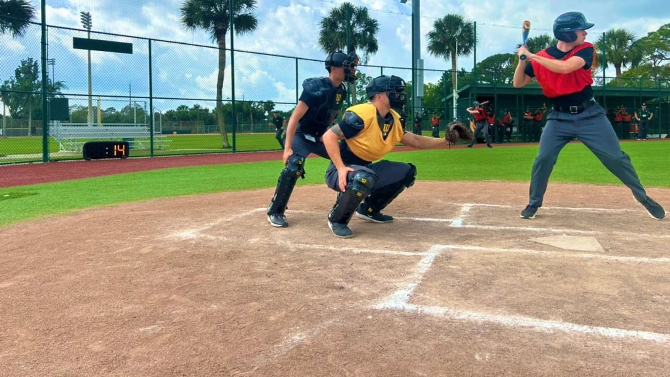 An umpire prospect stands with a pitch clock behind him and batter/catcher in front of him, ready to call balls and strikes.