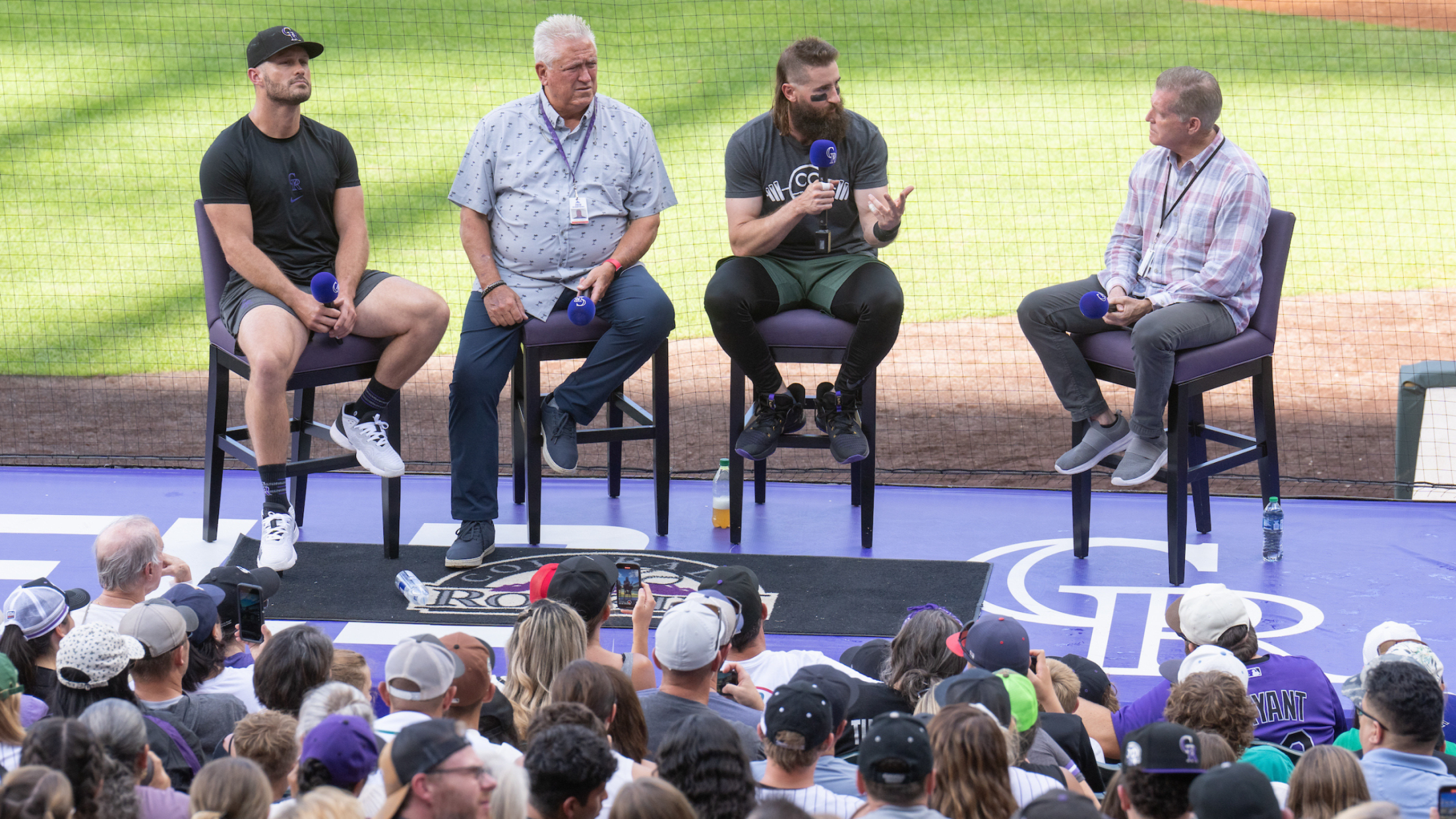 Players and coaches sitting on chairs on Colorado Rockies dugout facing fans in the stands