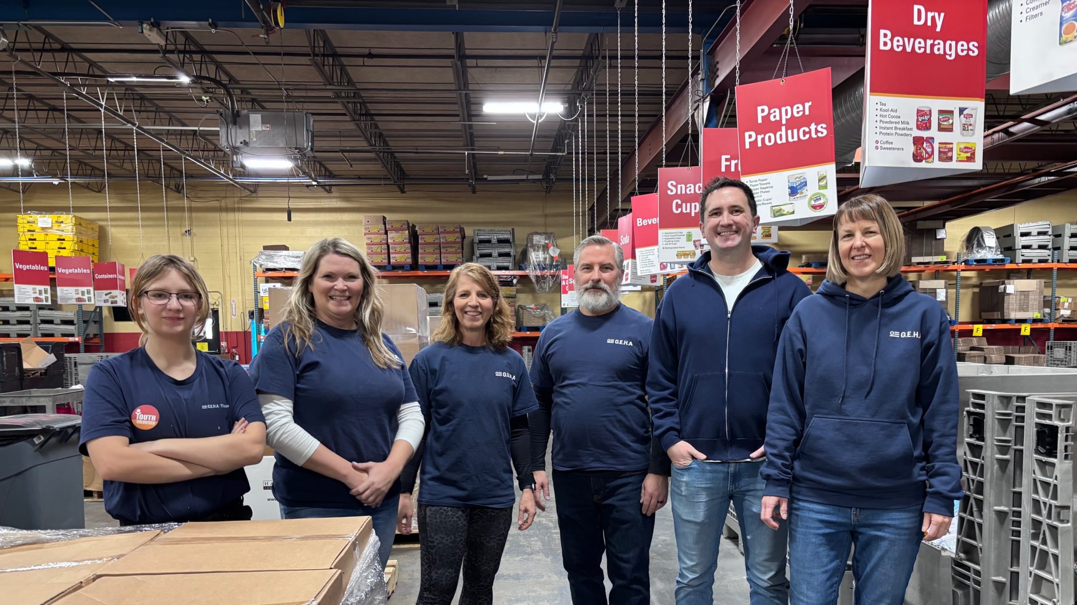 Volunteers stand in warehouse event by retail signs.