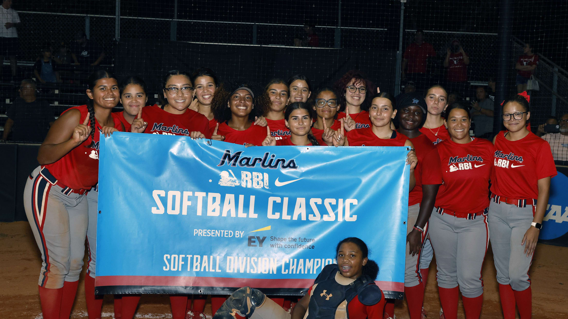 Players pose for a photo at home plate with the Marlins RBI Softball Classic banner.