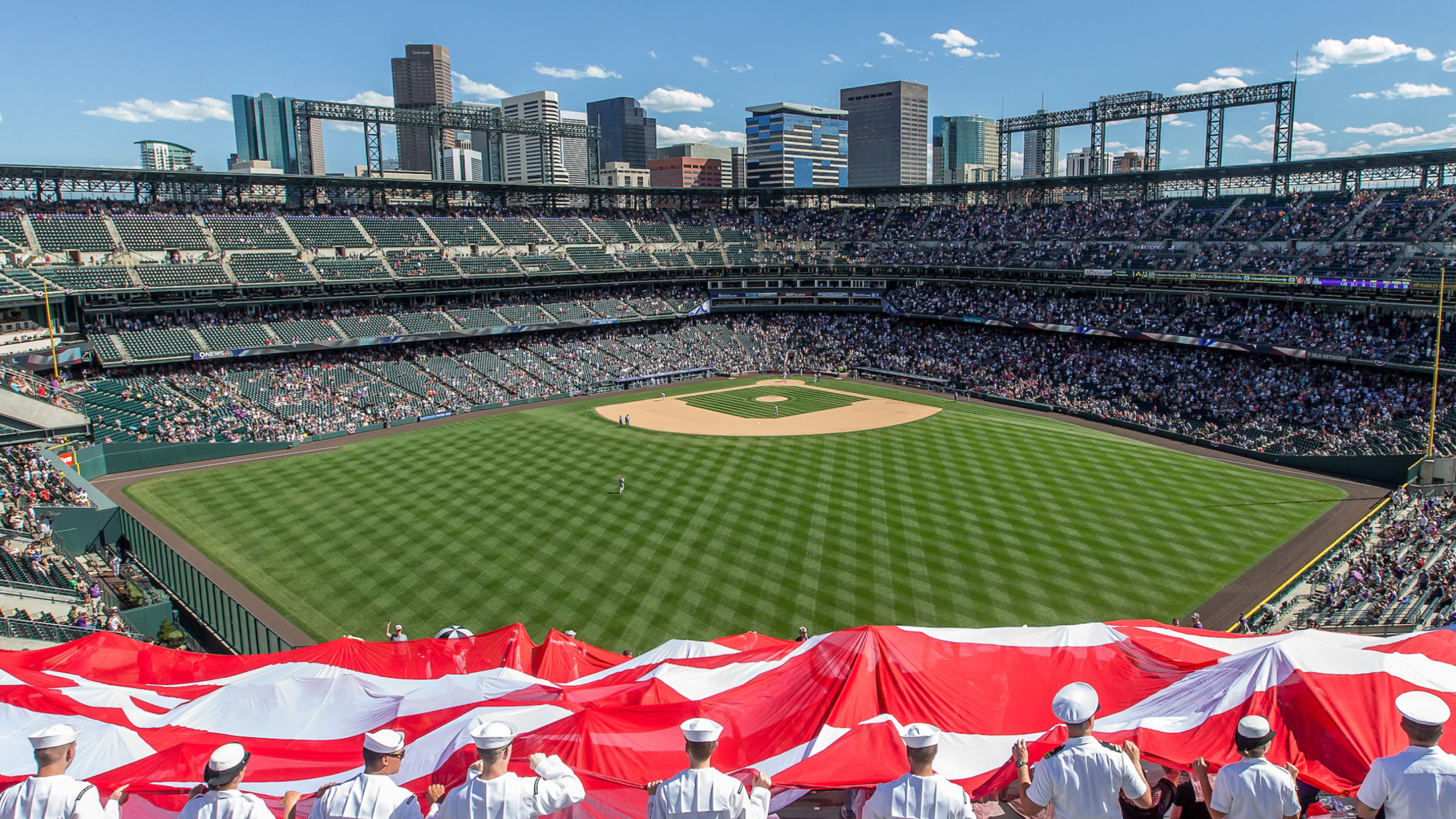 Service members holding American flag with field in background