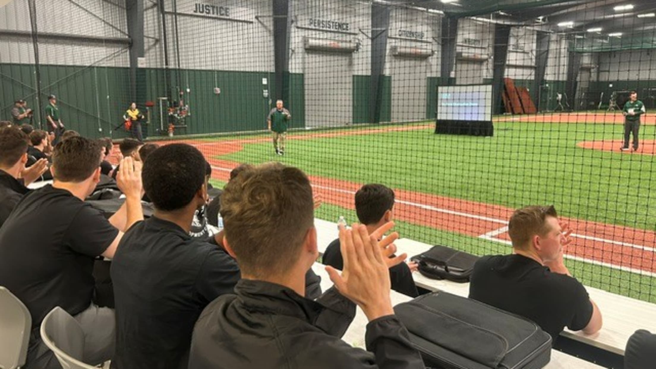 Umpires sit in multiple rows of seating watching a demonstration on the indoor field at the Robinson Training Complex.