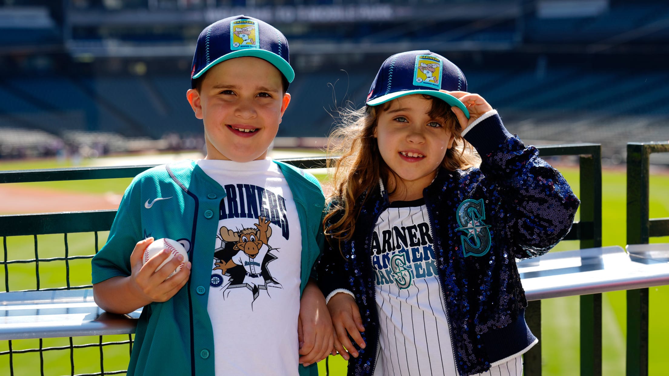 Two children smiling in Mariners Kids Club caps.