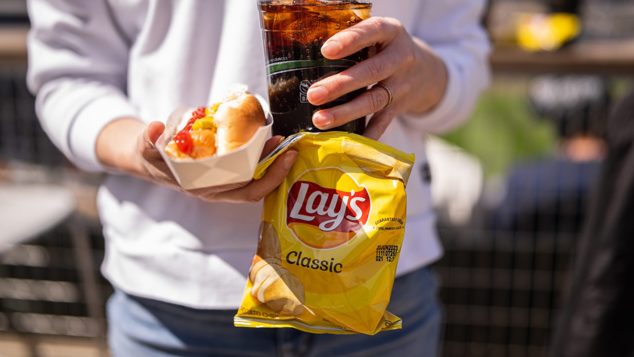 Person holding a hot dog, drink and bag of chips at Target Field.