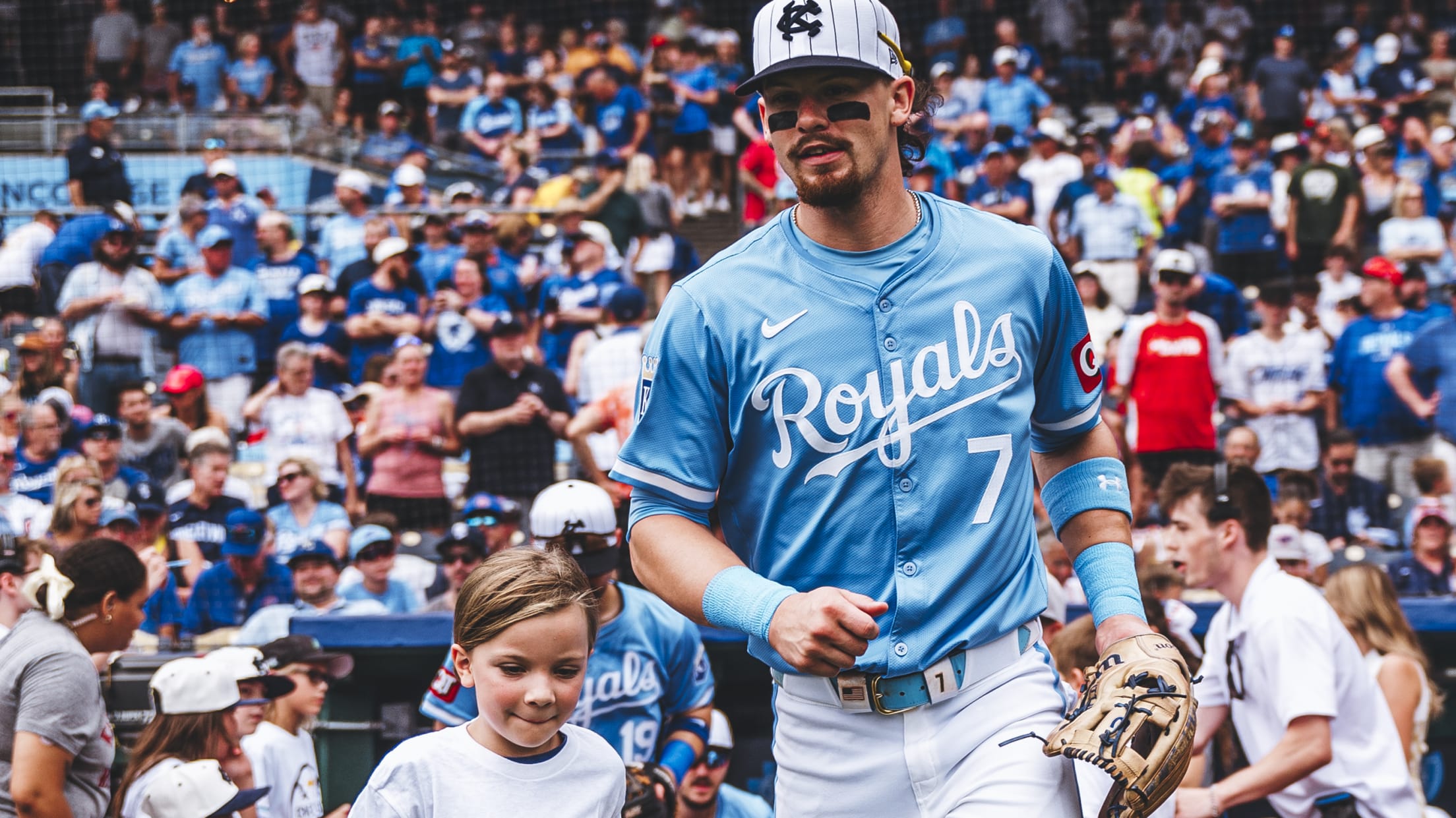 Bobby Witt Jr. takes the field with a young fan at Kauffman Stadium.