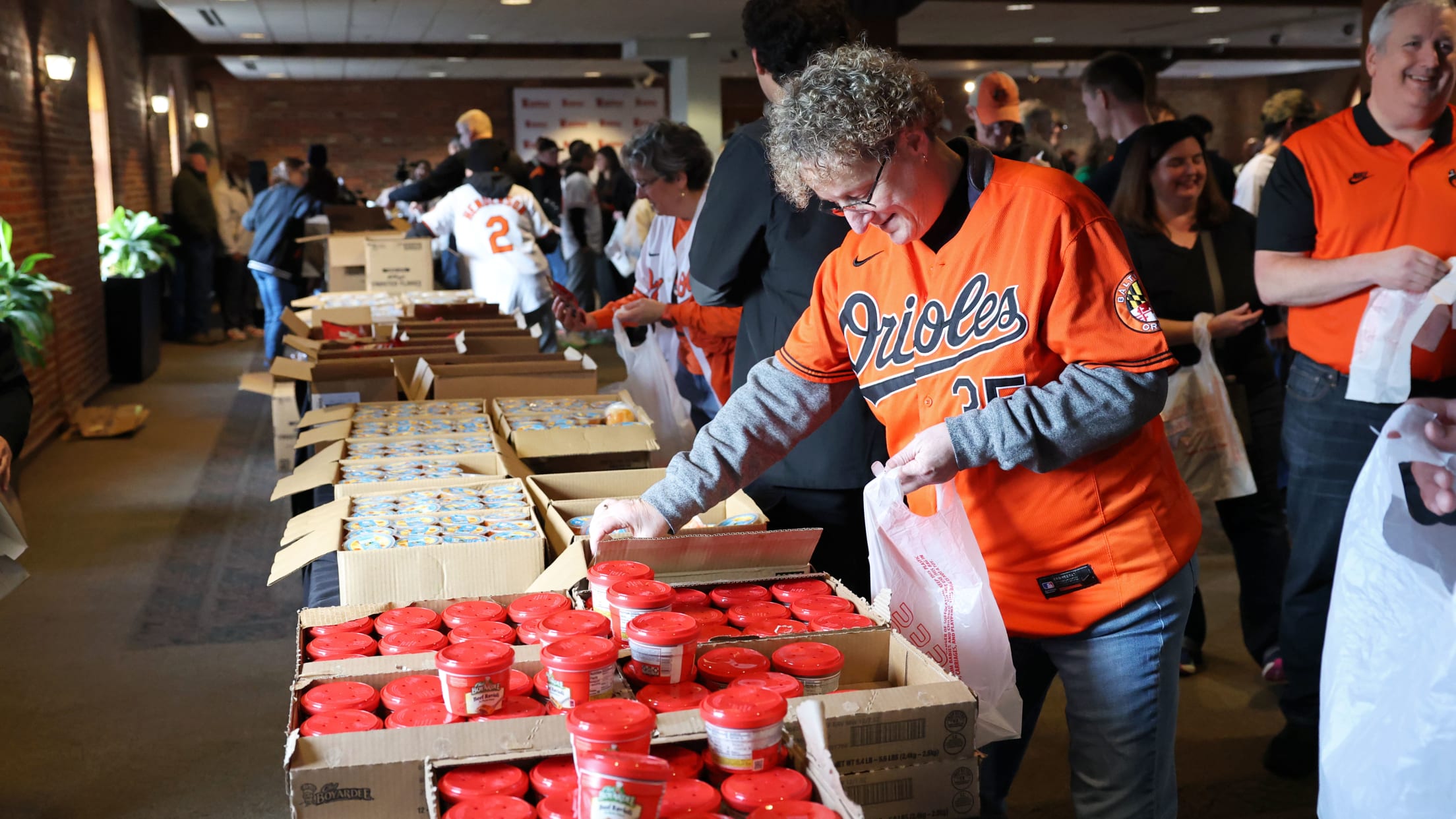 A volunteer in an Orioles jersey picks up canned food.