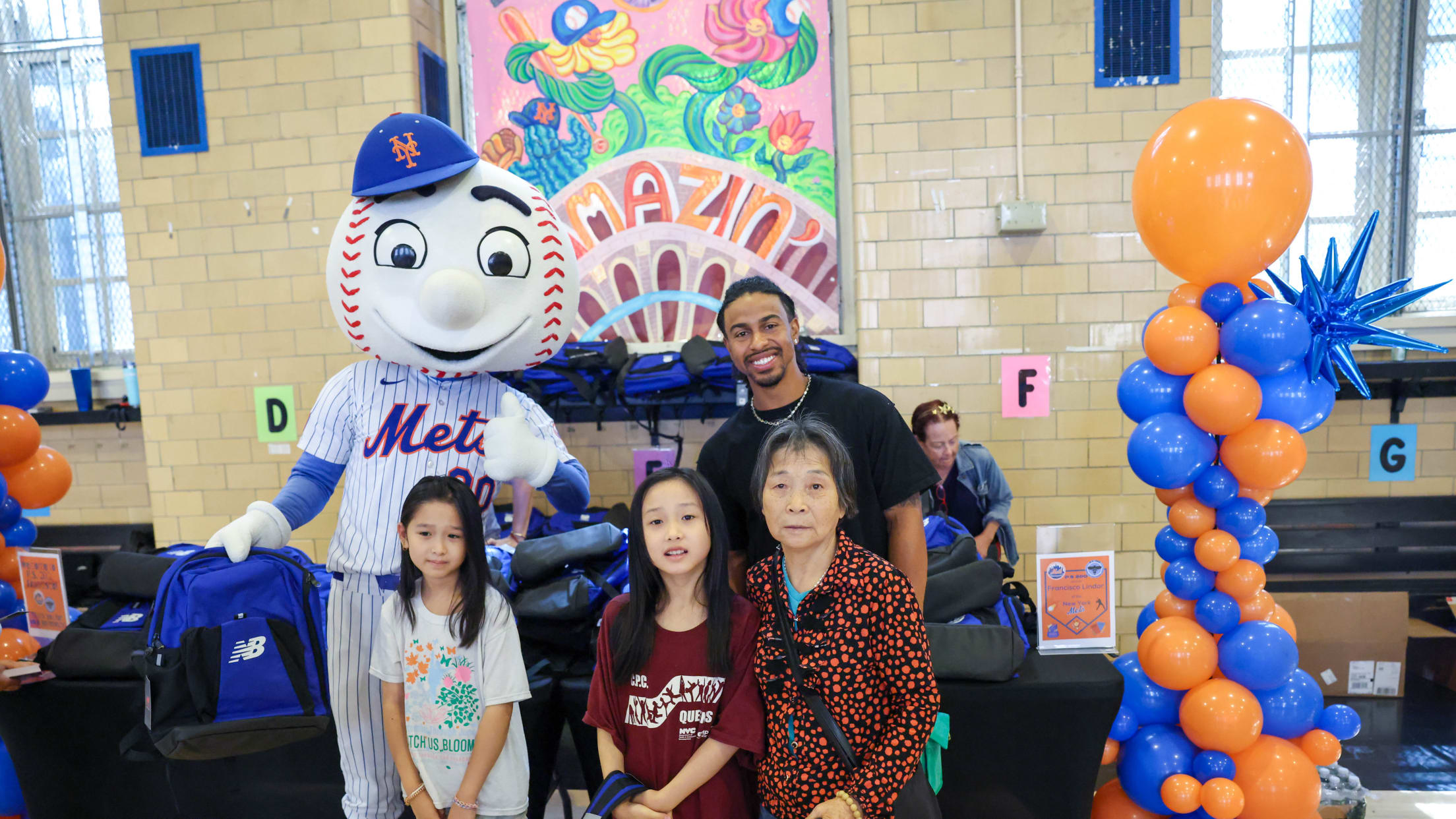 Francisco Lindor and Mr. Met take a photo with students and their families while receiving a backpack at a New York City school.