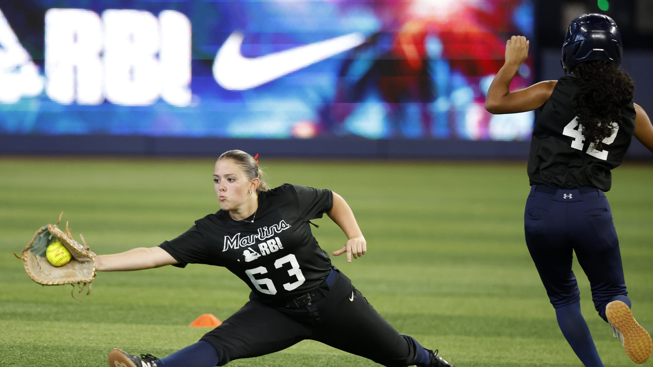 The first baseman stretches for the ball as a runner bears down on the base.