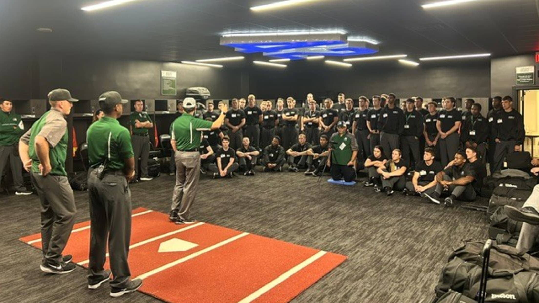 Umpires stand/sit at attention listening to a speaker indoors at the Robinson Training Complex.