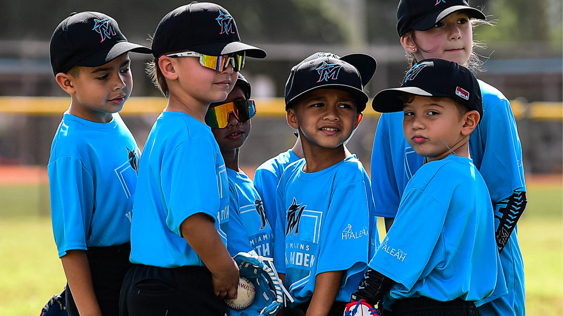 Miami Youth Academy athletes stand on a field with gloves.