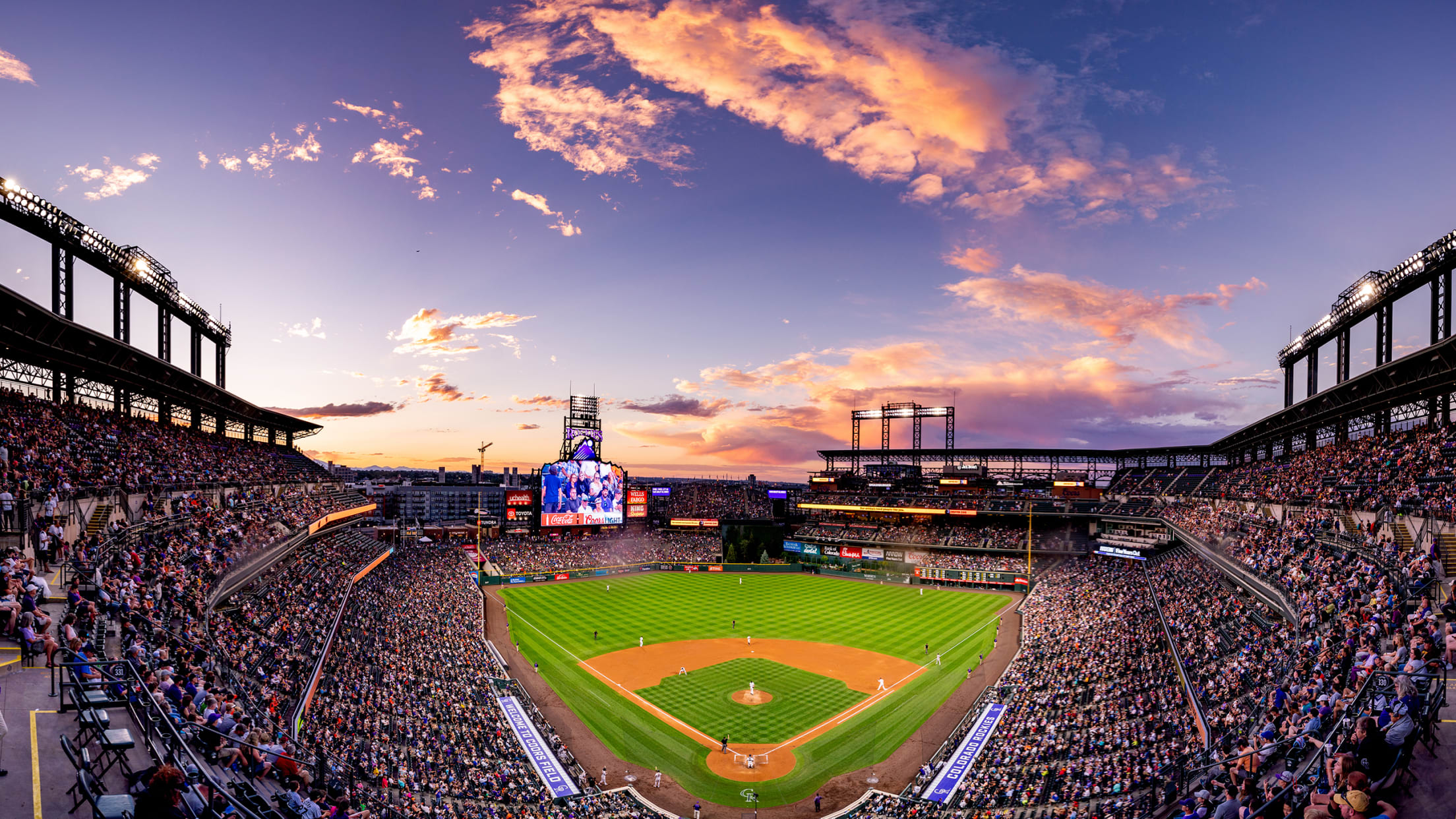 Coors Field at sunset, filled with a full crowd, watching the Colorado Rockies.