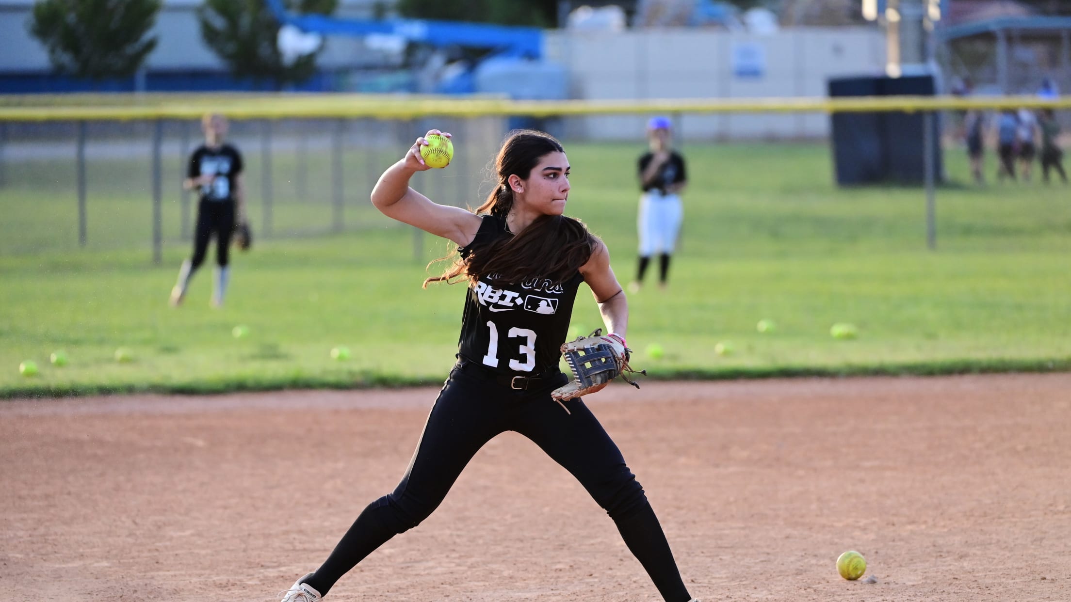 A softball player winds up to throw the ball from the infield dirt.