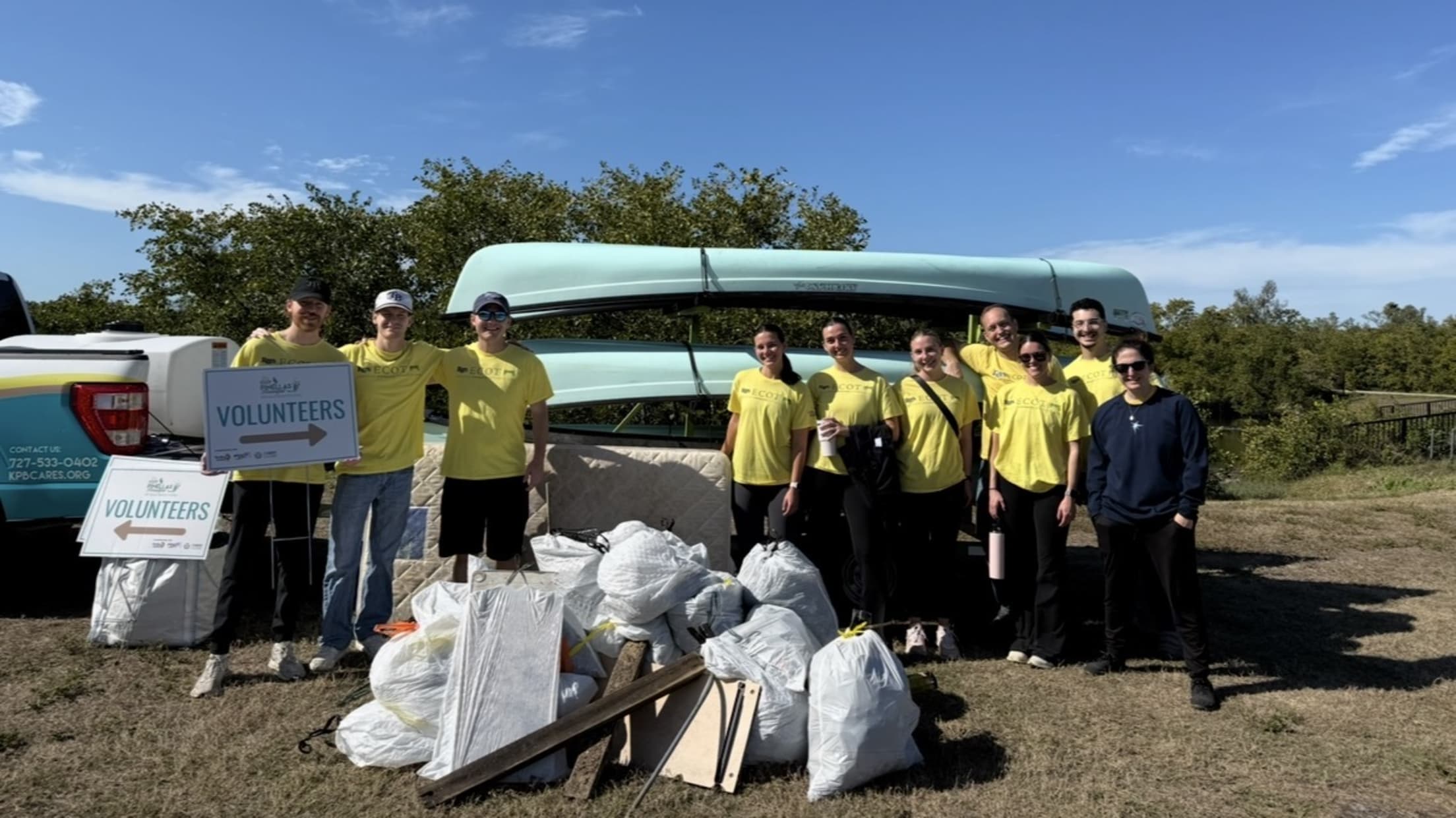 Volunteers pose outside at an event in front of canoes.