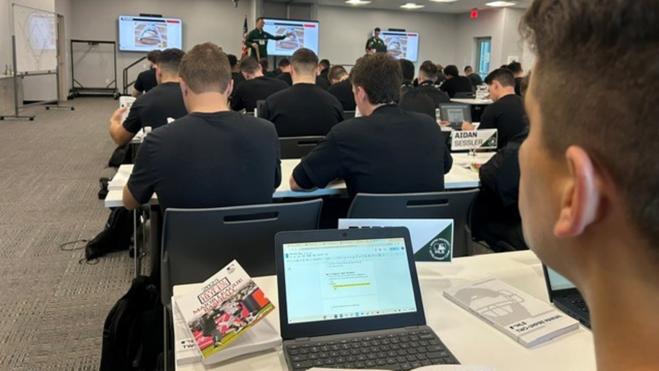 Umpires with laptops/tablets in front of them sit in a class at the umpire prospect camp.