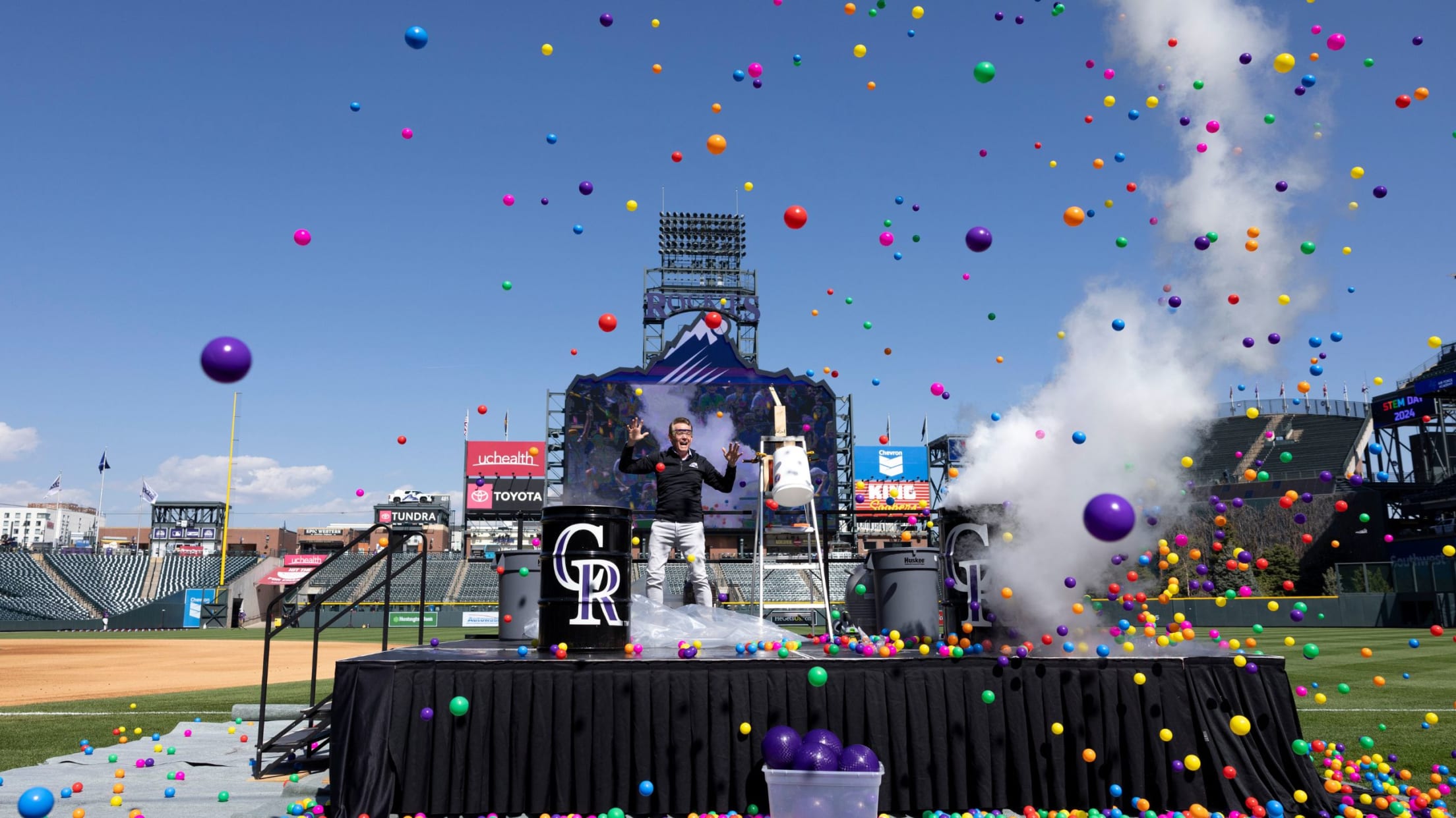 Steve Spangler on stage on the playing surface at Coors Field with colored plastic balls flying through the air