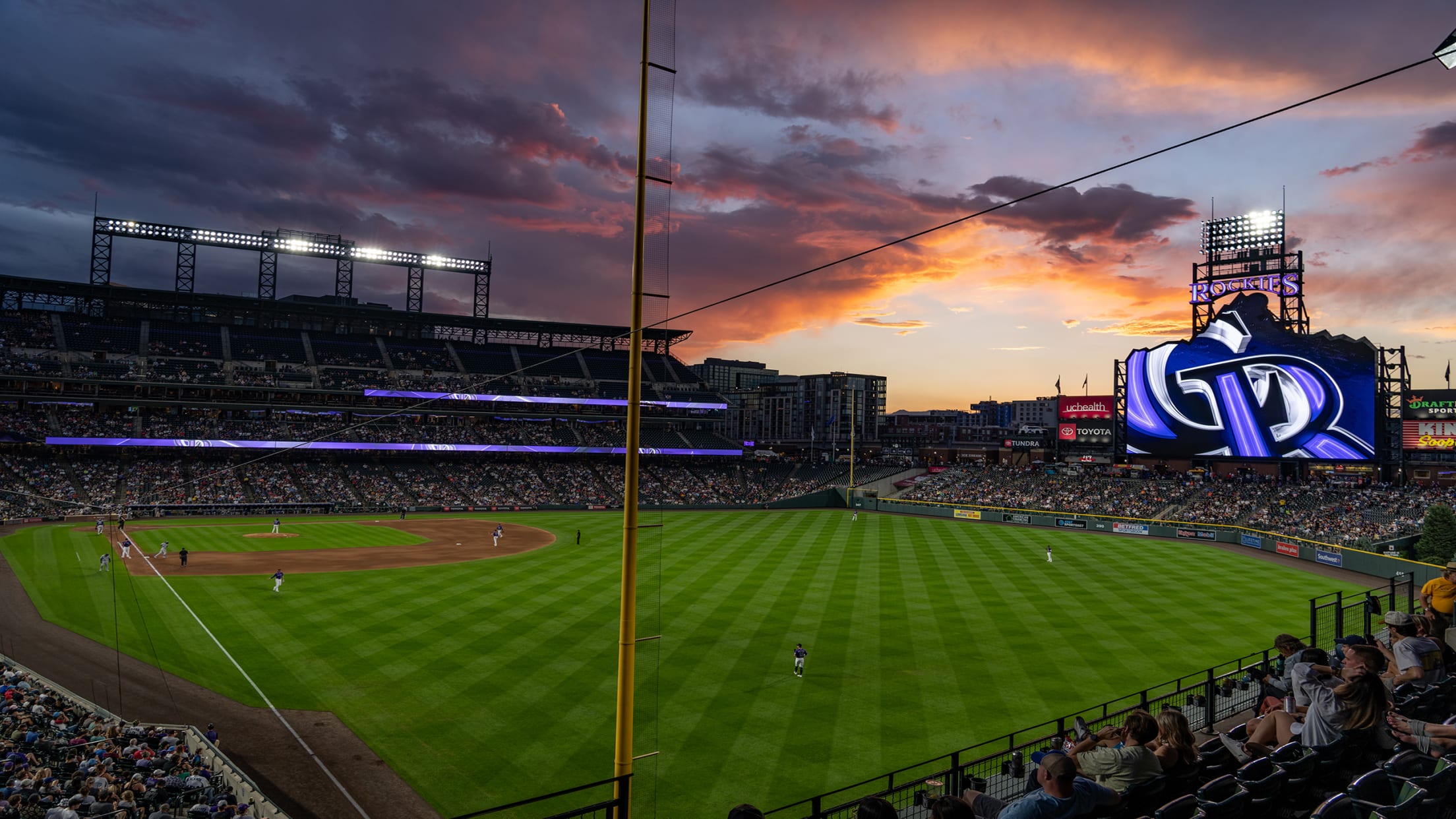 View from foul territory during a game with the sun setting next to the scoreboard