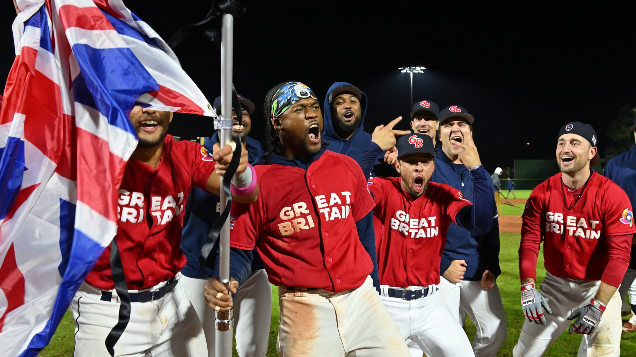Players for Team Great Britain celebrate with a British flag on the field after a walk-off win against Spain in Regensburg.