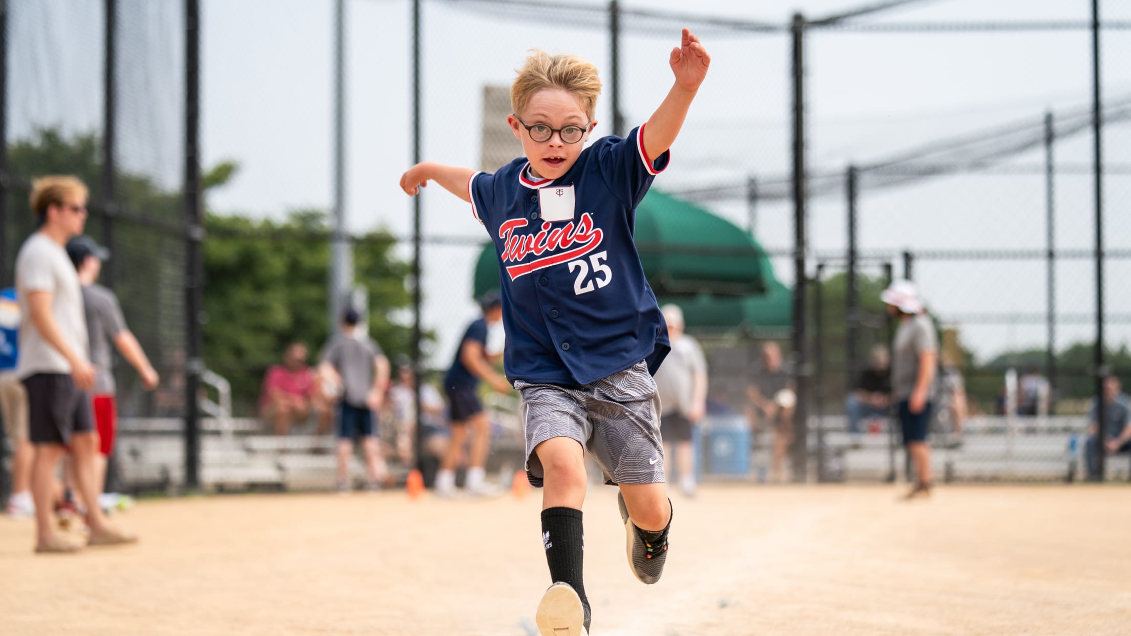 A boy looks at the camera as he runs to first base on a ballfield.