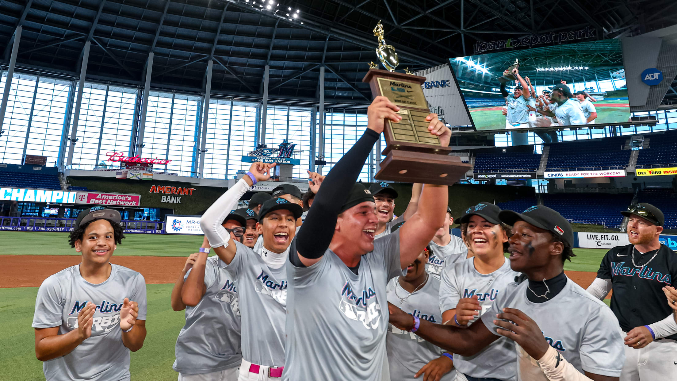 The winning team celebrates with their trophy on the field at LoanDepot Park during the Marlins Nike RBI Wood Bat Championship.