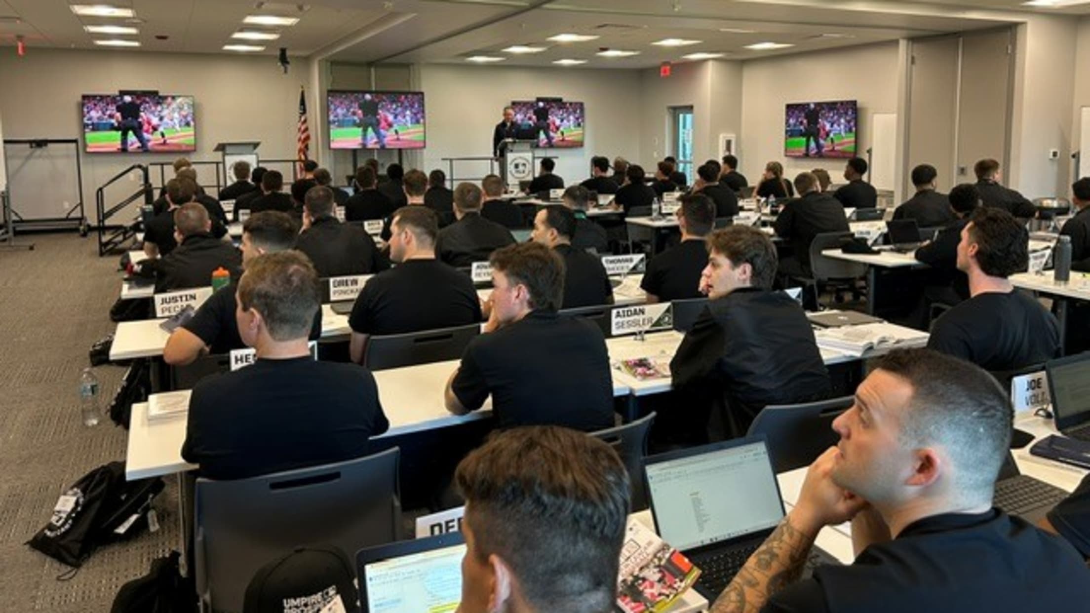 Umpires with laptops/tablets in front of them sit in a class at the umpire prospect camp.