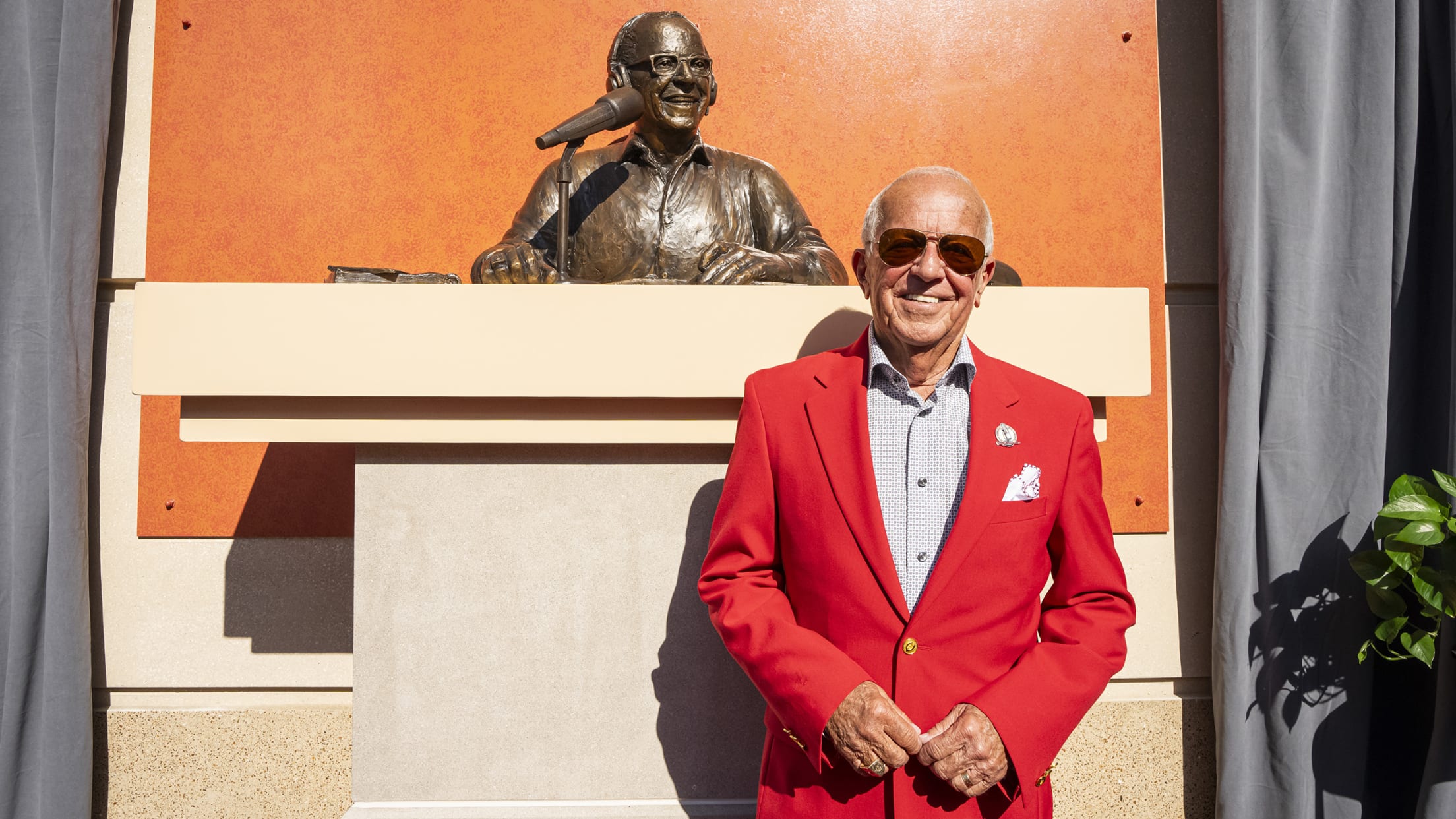 Marty in front of his statue in sharp red suit and sunglasses.