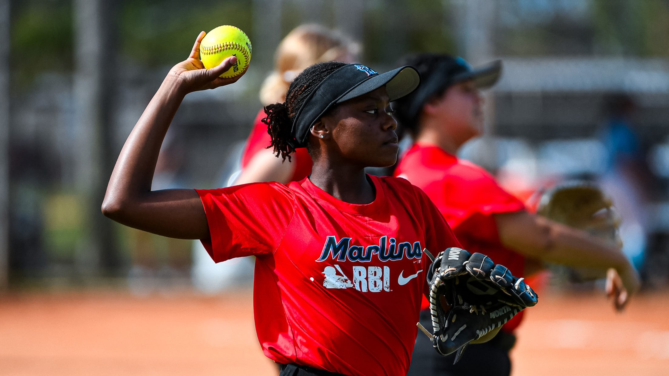 A Marlins RBI athlete throws a softball on a field.