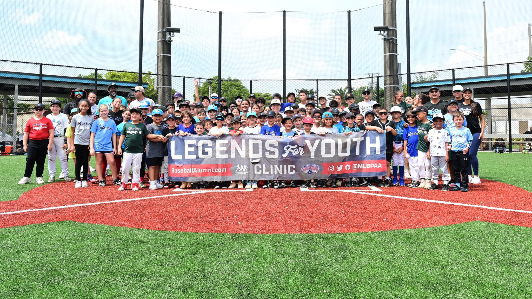 Players, coaches and legends pose for a group photo behind a Legends for Youth Clinic banner.