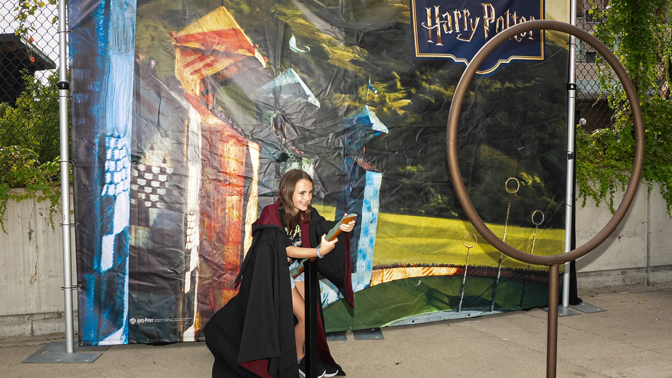 Young fan posing on broom in front of Quidditch photo backdrop.