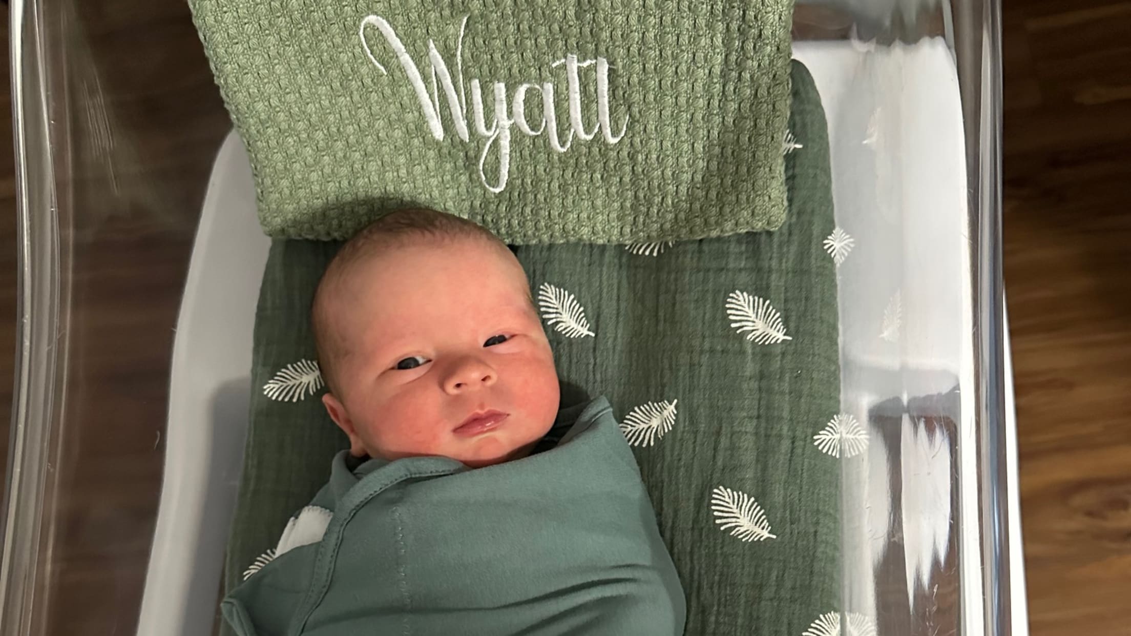 A baby lays in a crib underneath a towel with their name "Rayden Wyatt" on it.