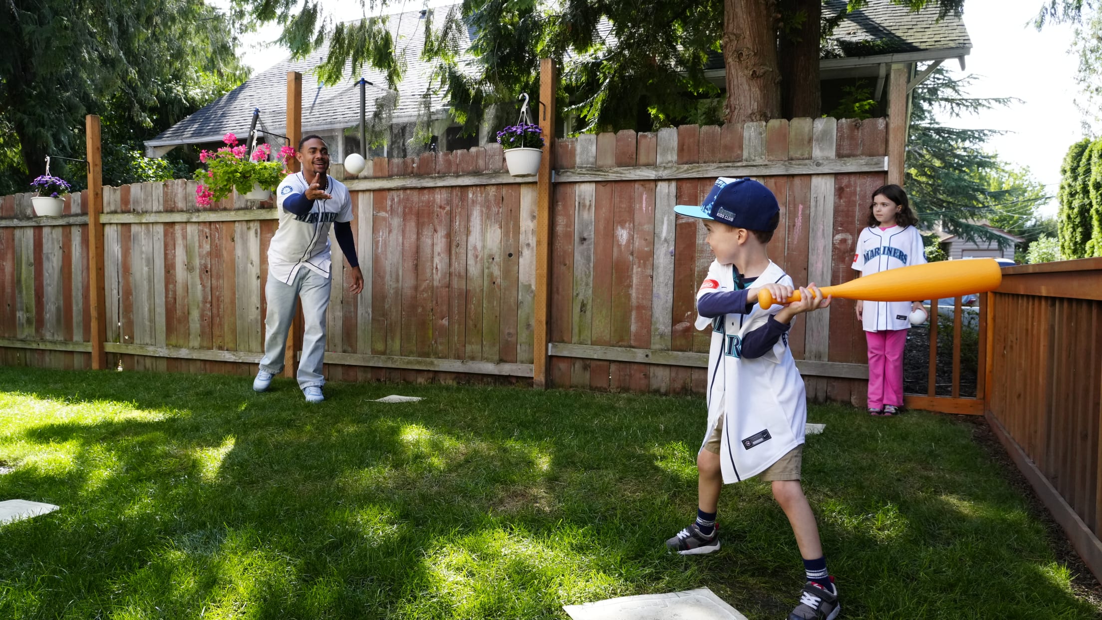 Julio Rodriguez plays baseball with a child in a yard.