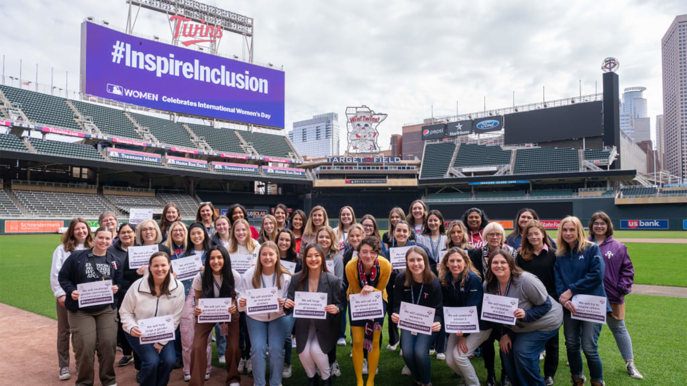 Twins employees standing on Target Field, with #InspireInclusion on the scoreboard in the background.