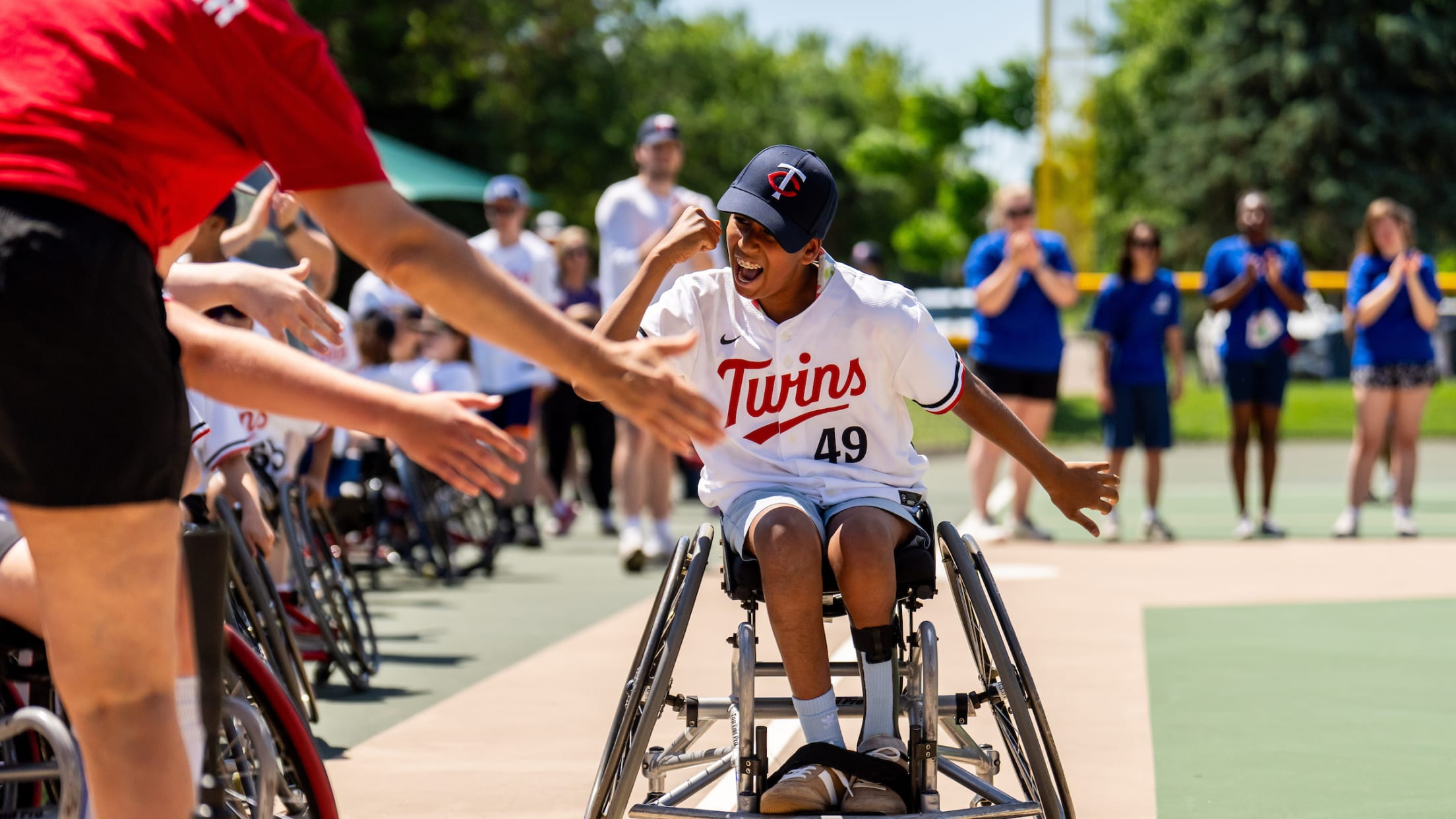 A boy using a wheelchair smiles and pumps his fist as he gets ready to cross home plate on an adaptive ballfield.