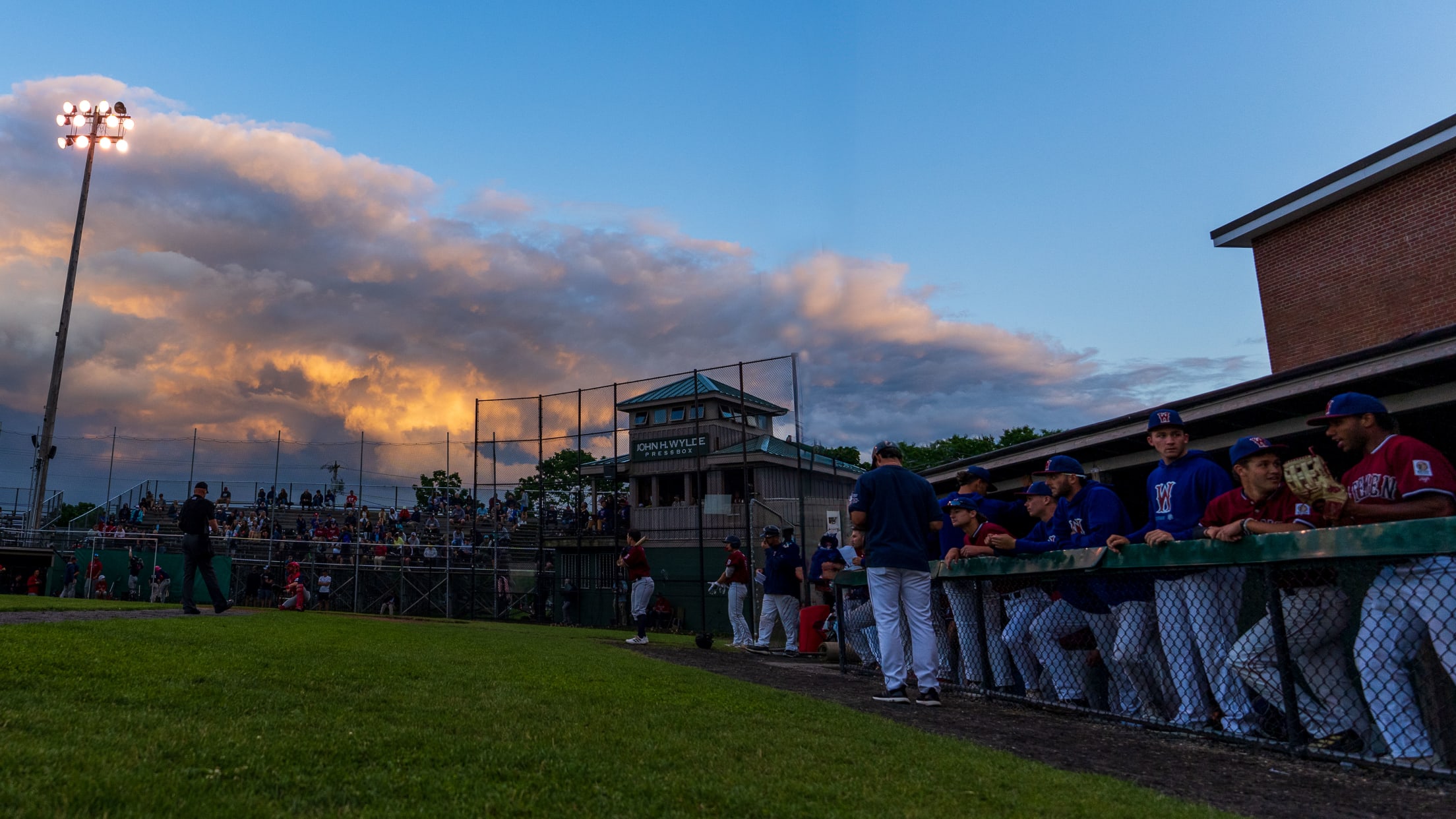 The sun begins to set above Spillane Field as the Gatemen players stand in the dugout.