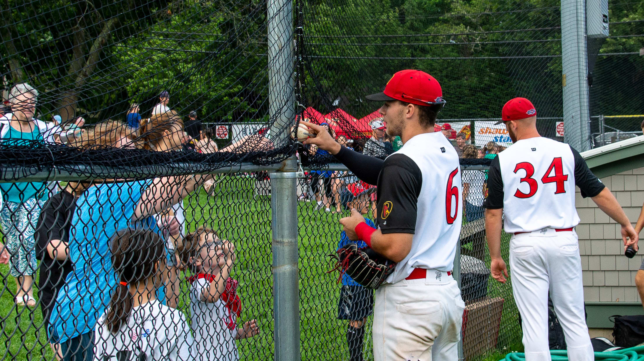 Orleans Firebirds player passes a signed baseball around the fence to a fan.