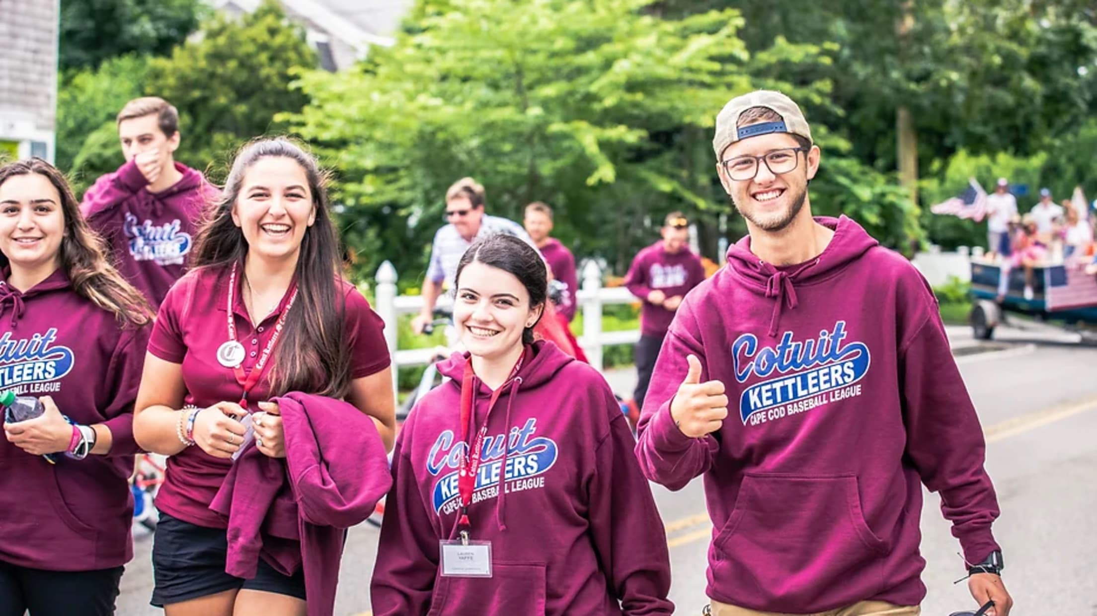 Four Kettleers staffers in burgundy Cotuit sweatshirts smile at the camera while walking on a street.