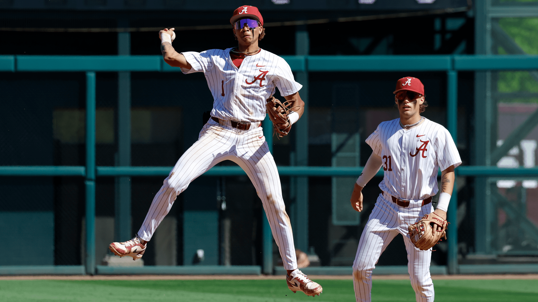 Alabama infielder Justin Lebron throws a ball to first base while in midair while his teammate looks on.