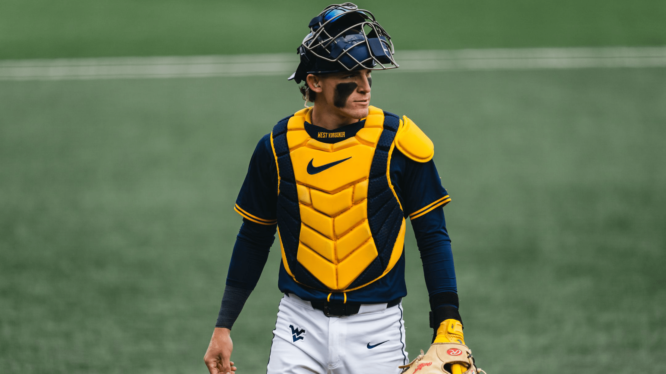 West Virginia's Gavin Kelly walks off the field, wearing catcher's gear