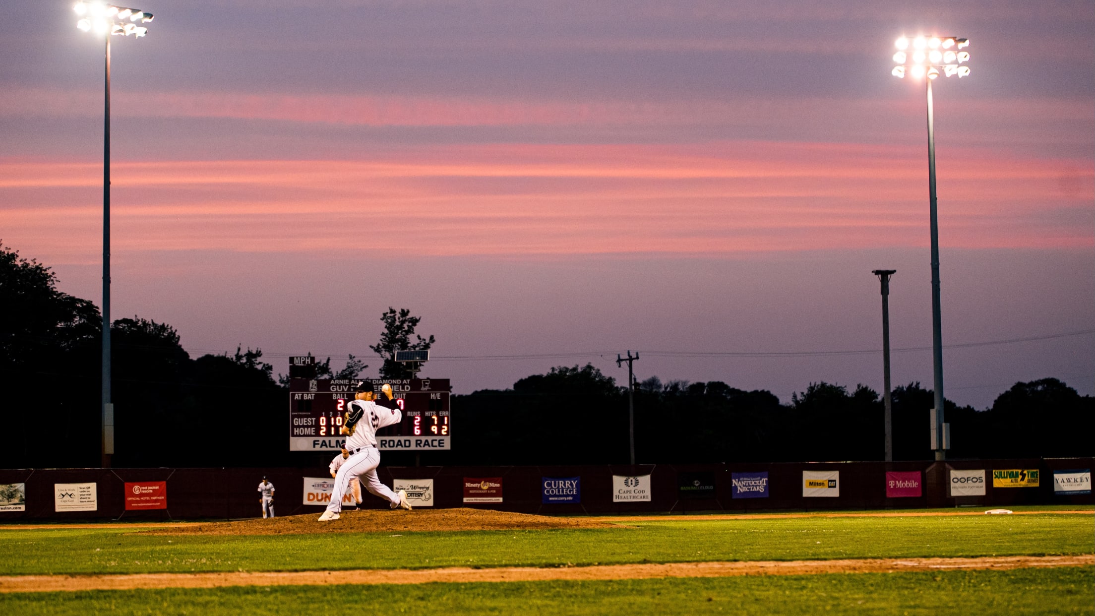 Falmouth pitcher in mid-pitching motion as the sun sets in an blue/orange combo above the stadium.