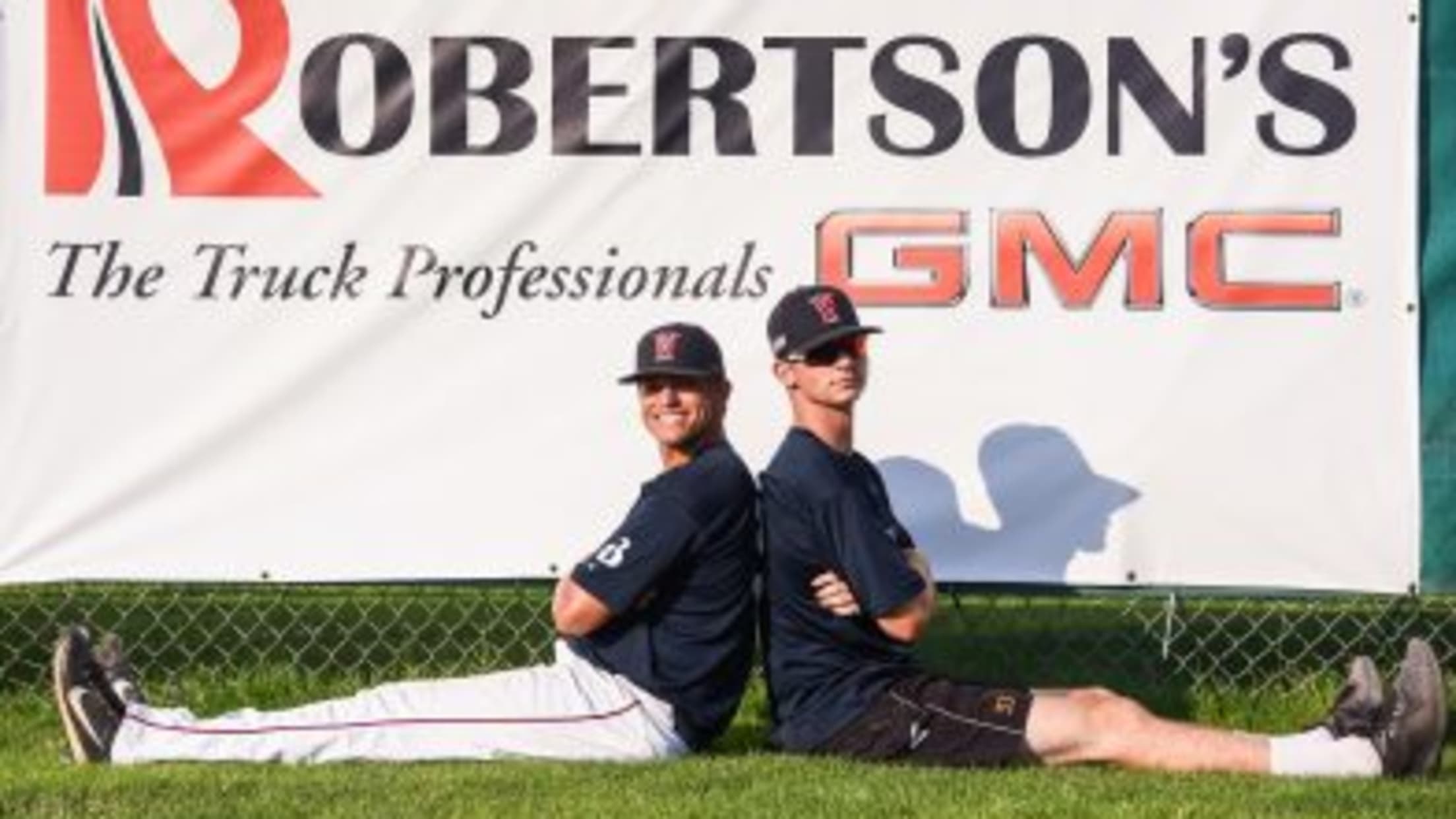 Two Wareham players sit on the field back-to-back, posing in front of a Robertson's advertisement in the outfield.