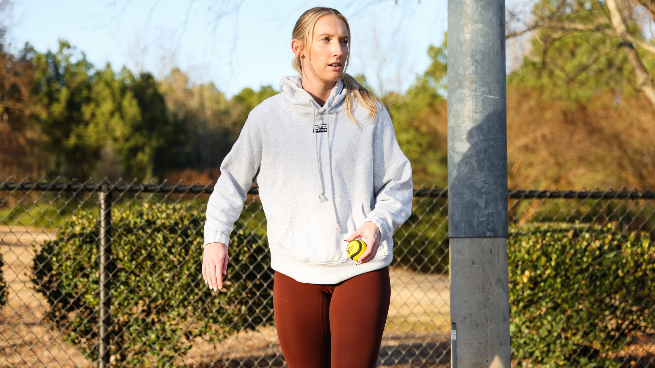 Woman in front of a fence holds a yellow Baseball5 ball.
