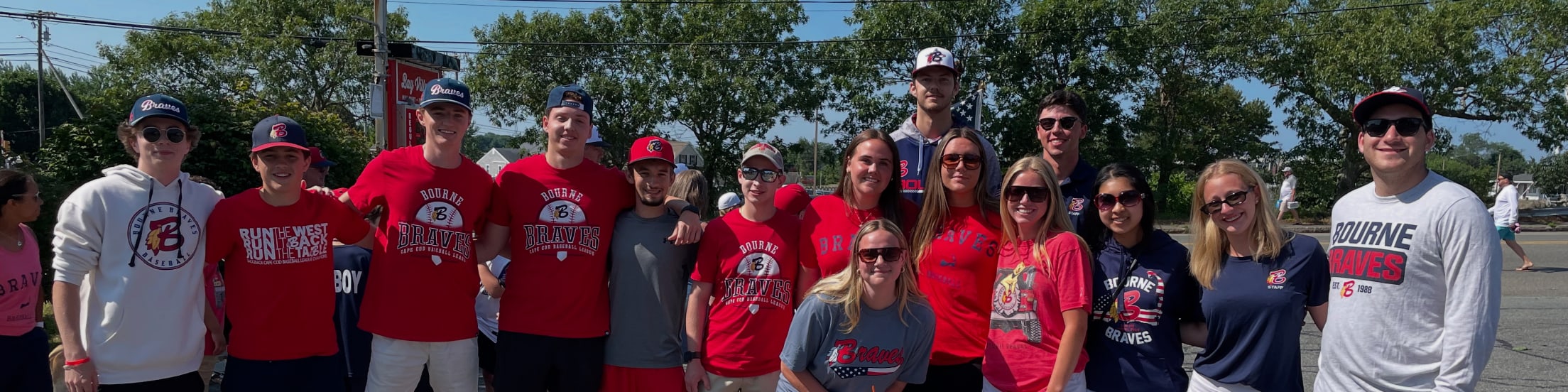 A group of people in Bourne Braves apparel pose for a photo in a parking lot.