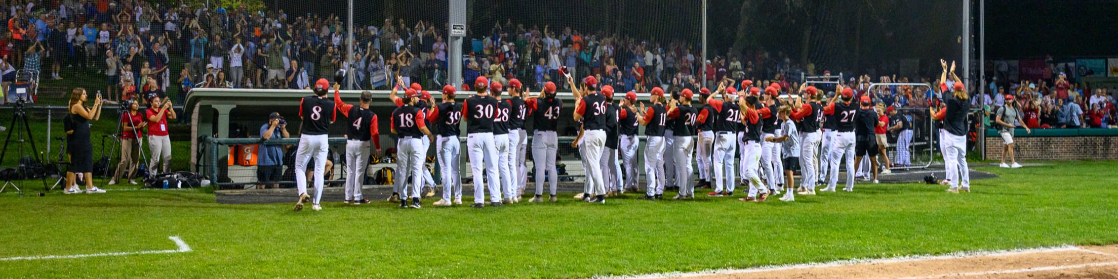 Orleans Firebirds players stand in front of their dugout and doff their caps towards/clap for their fans.