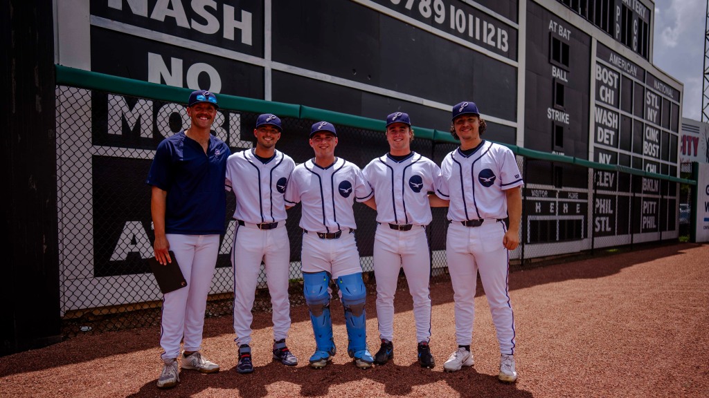Wearing throwback Pensacola Seagulls uniforms, Blue Wahoos players gather at iconic scoreboard at 116-year-old Rickwood Field.