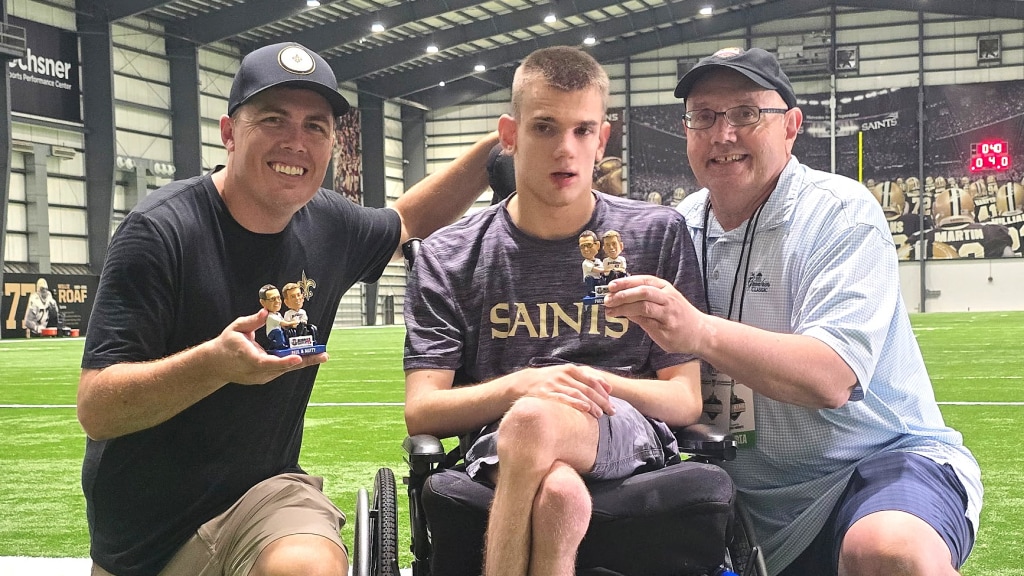 New Orleans Saints head coach Kellen Moore visits with Matthew Chestnutt and his father Paul in helping bring awareness to his bobblehead night during a Saints training camp practice.