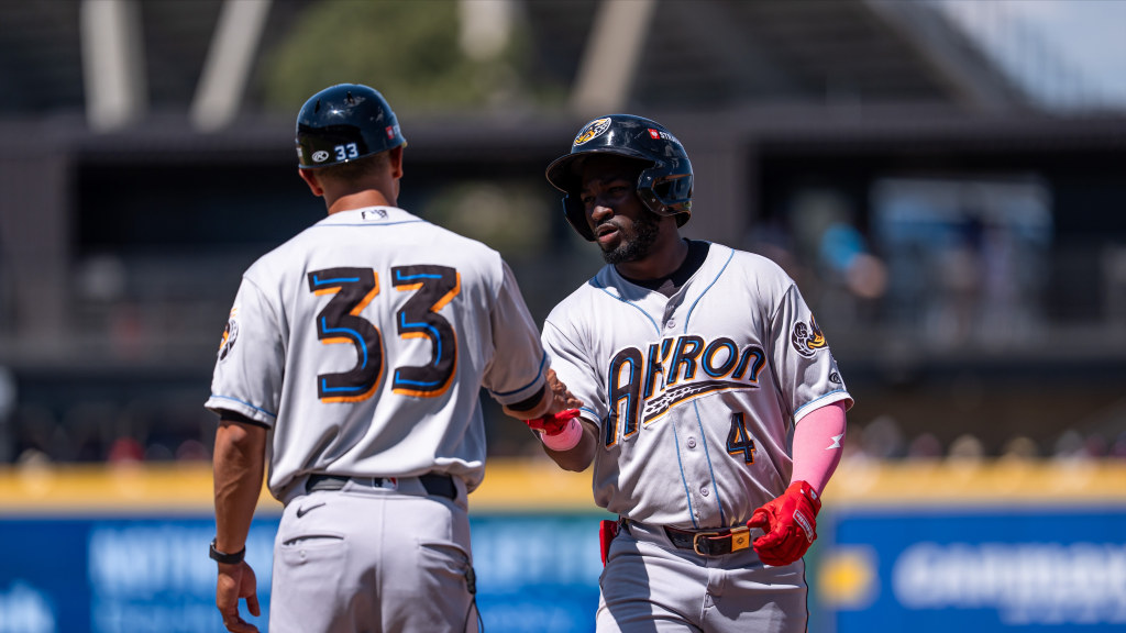 Akron first base coach Yan Rivera (33) congratulates Wuilfredo Antunez (4) after his fourth-inning single for Akron's first hit on Sunday.