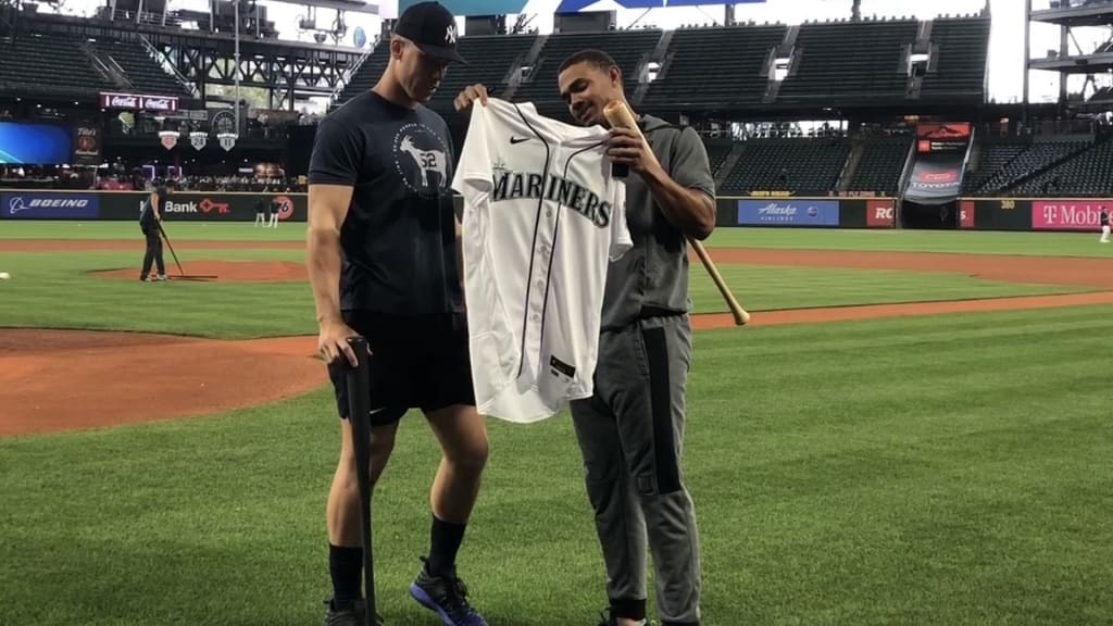 Aaron Judge, in shorts and T-shirt, looks at a Mariners jersey held by Julio Rodriguez, in a workout suit, holding a bat beneath his left arm