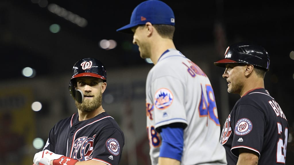 Washington Nationals' Bryce Harper, left, stands on the field next to New York Mets starting pitcher Jacob deGrom, center, after he grounded out during the sixth inning of a baseball game Friday, Sept. 21, 2018, in Washington. At right is Nationals first base coach Tim Bogar at right. The Mets won 4-2. (AP Photo/Nick Wass)