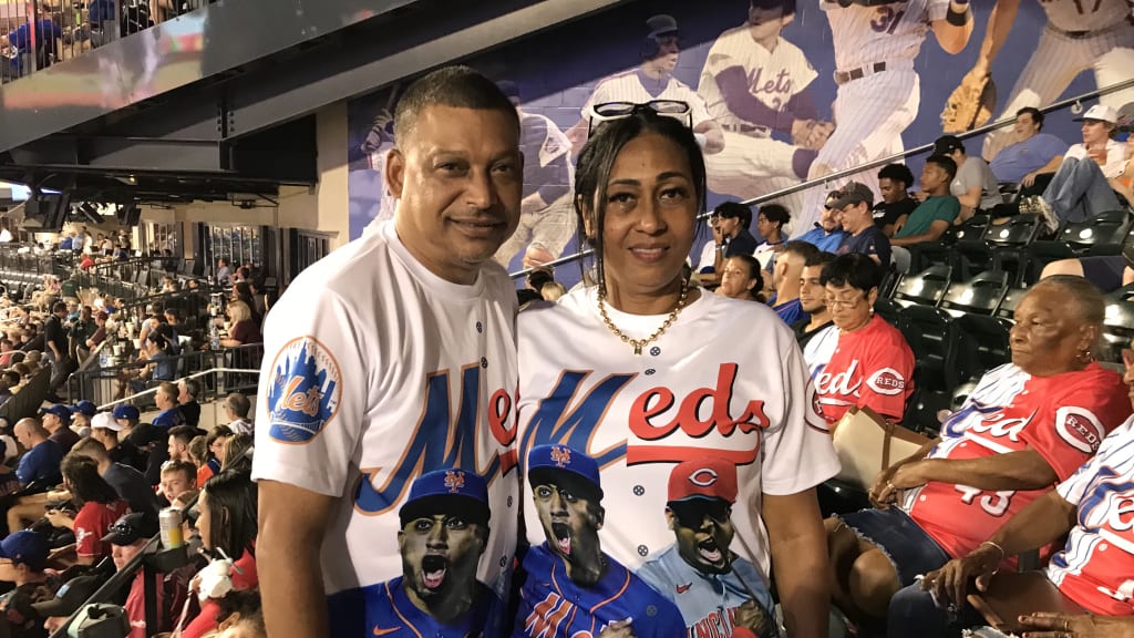 Two fans in the crowd with jerseys showing a Mets player on the left beneath the ''M'' in the team name and a Reds player on the right beneath the ''e-d-s''